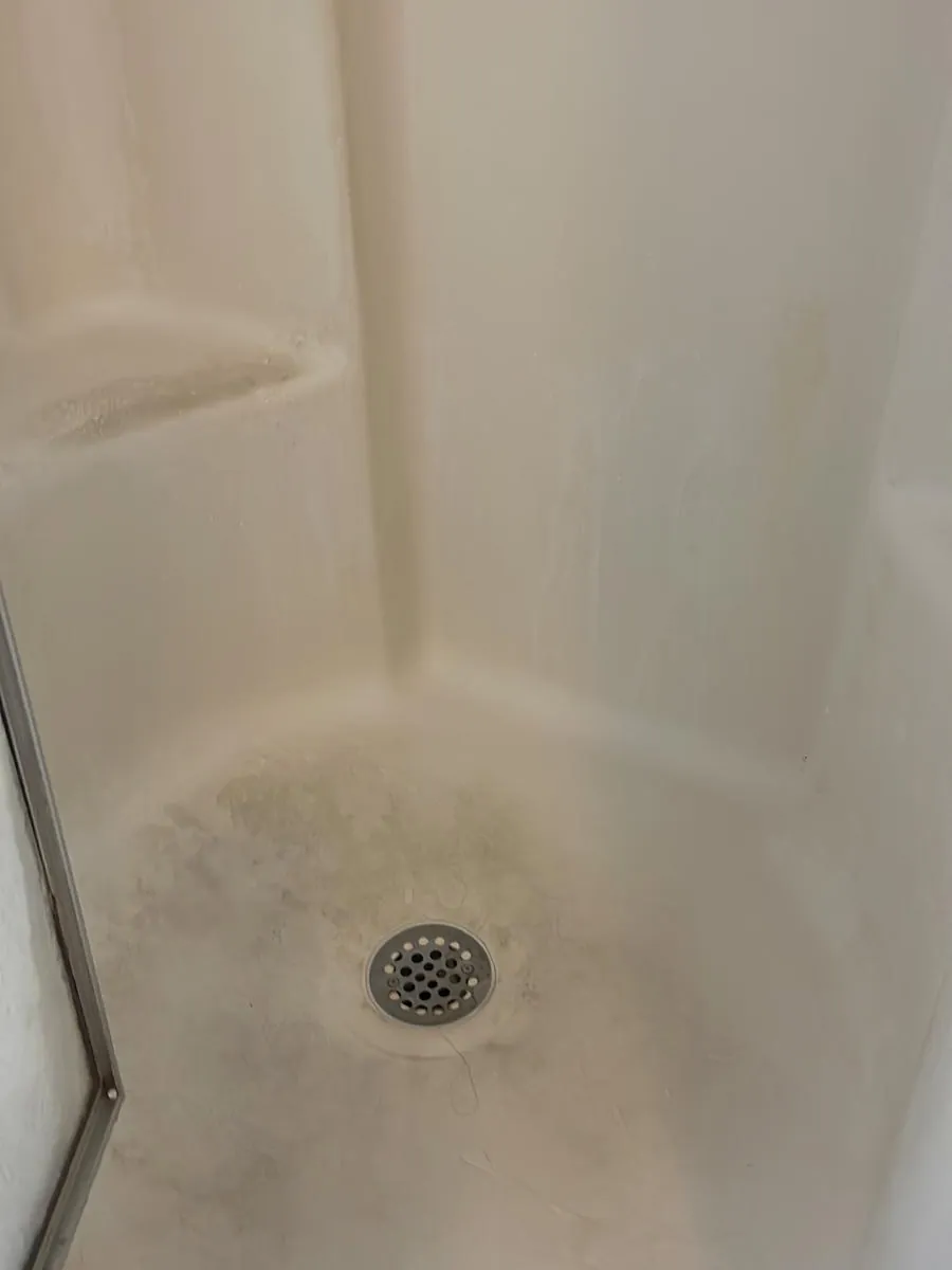 Shower pan and drain before deep cleaning in Clinton, MA, with mildew around the drain